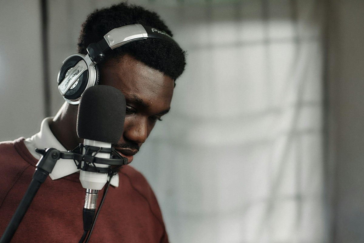 A voice performer wearing headphones records at a studio microphone